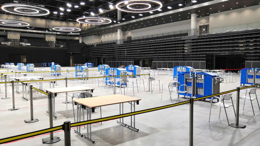 A vaccine center with rows of tables and stations that include Ecolab solutions, such as wipes, hand rub and spray surface disinfectant.