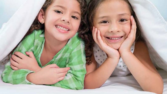 Image of two children in bed with clean sheets over them.