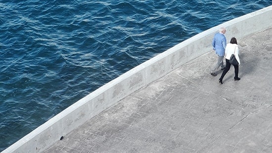 Aerial view of two individuals walking on concrete pathway above large body of water.